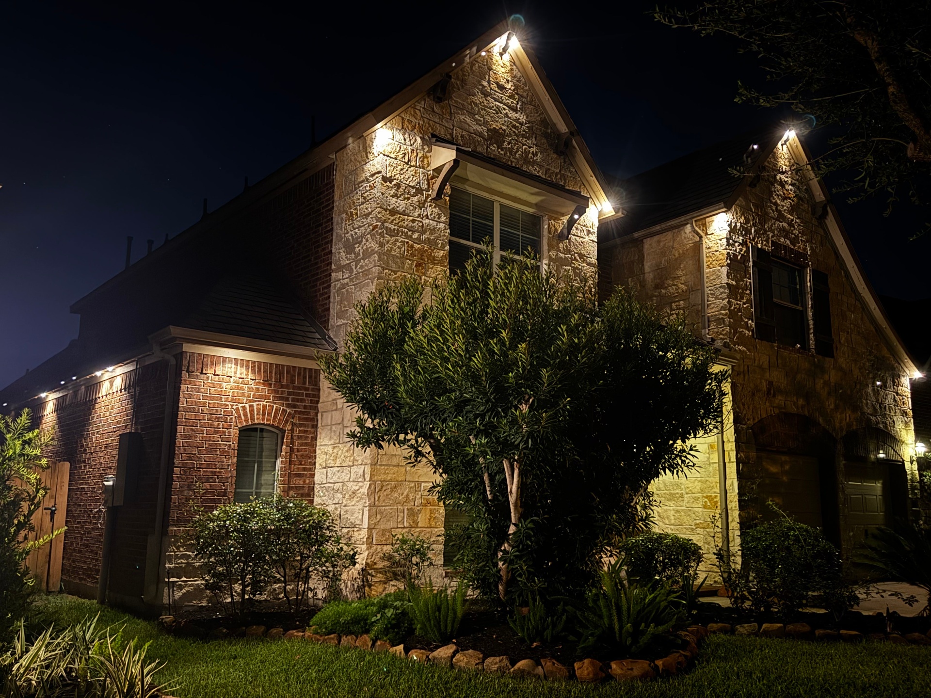 Stone home with warm white uplighting and roofline accents