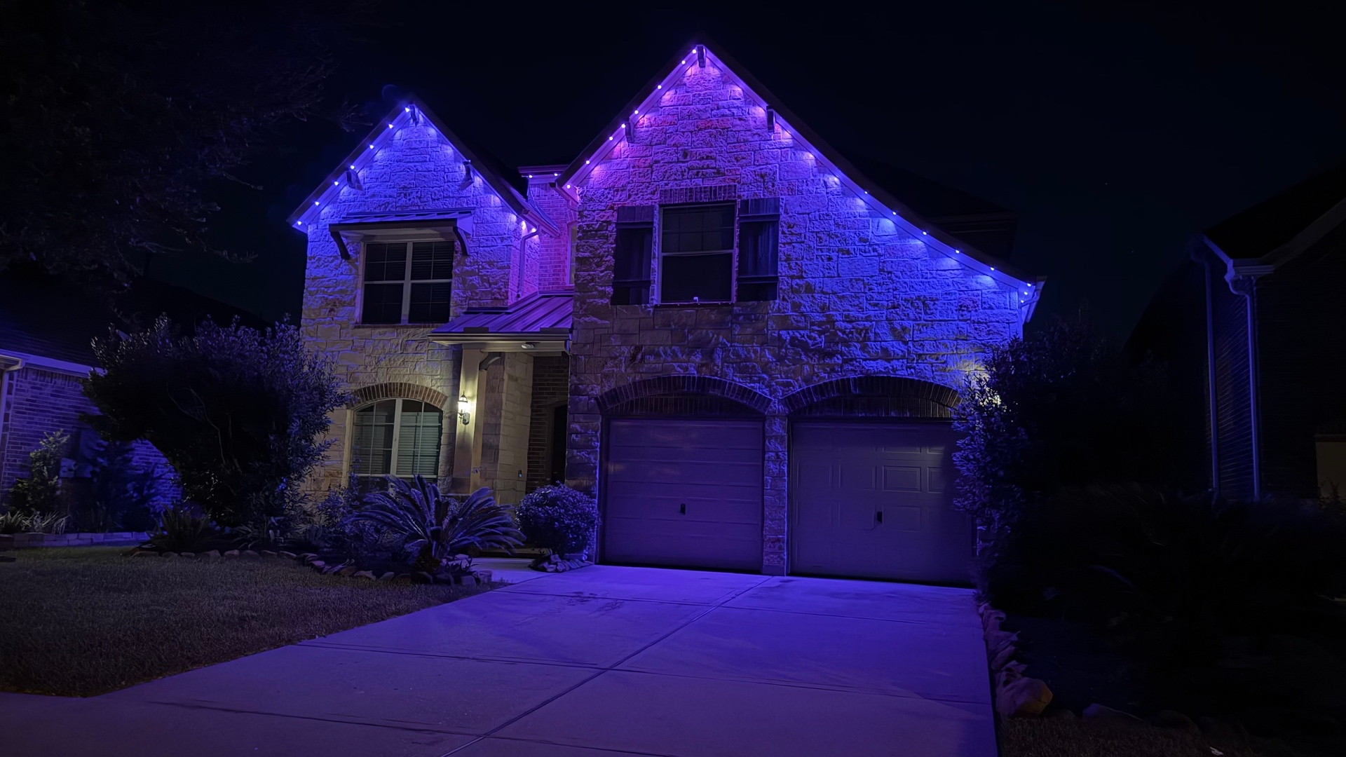 Stone home lit with blue and purple permanent LED roofline lighting at night